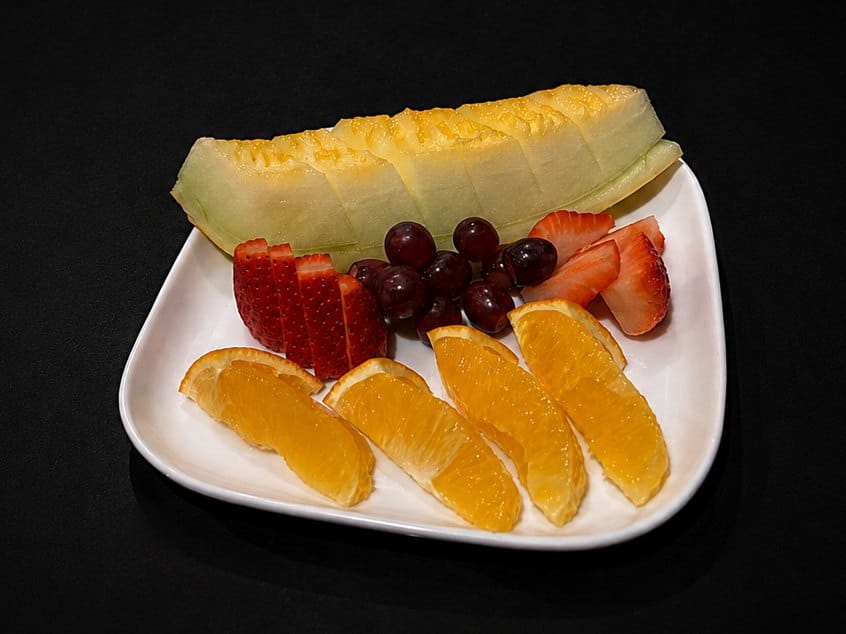 A plate of seasonal fruit: melon, orange, strawberries and grapes